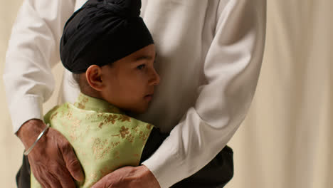 Nahaufnahme,-Studioaufnahme-Eines-Jungen-Sikh-Jungen-Mit-Turban-Und-Haarknoten,-Der-Seinen-Großvater-Vor-Einfarbigem-Hintergrund-Umarmt-1